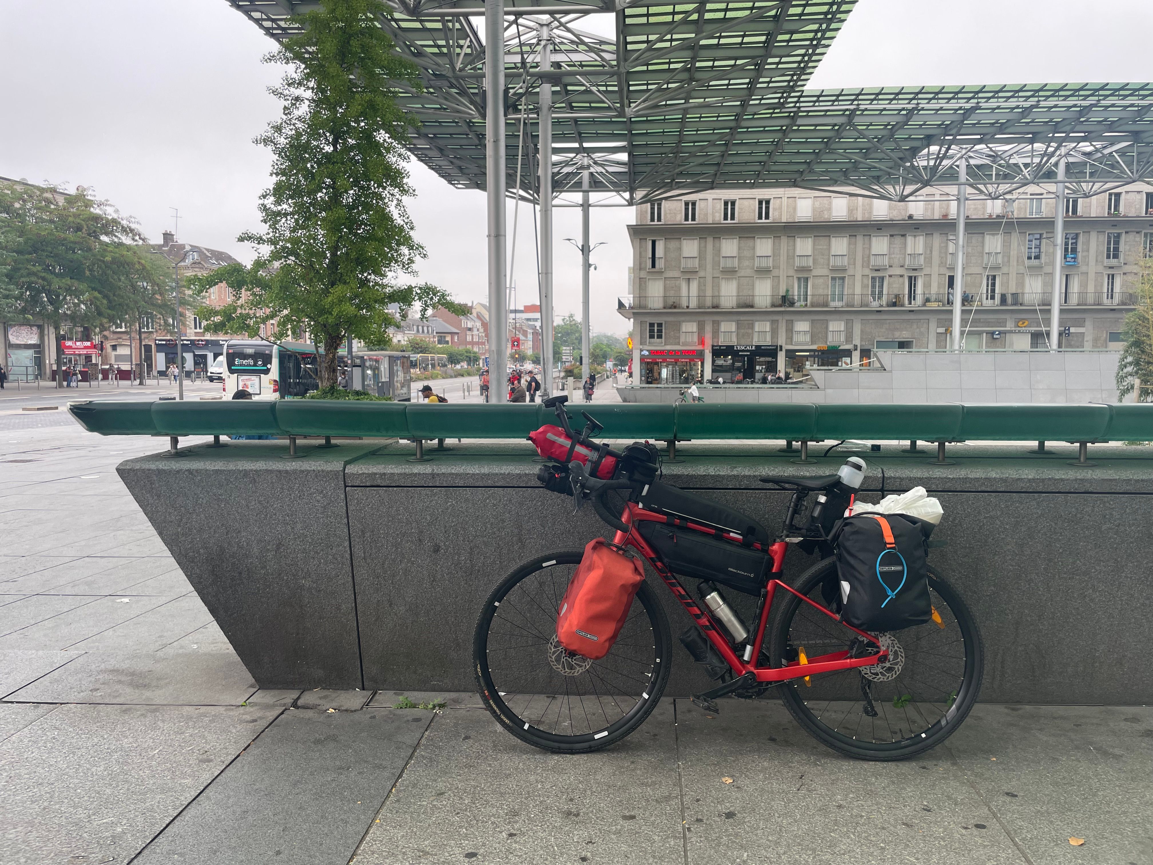 Un vélo rouge, vu de coté, chargé de sacoches.