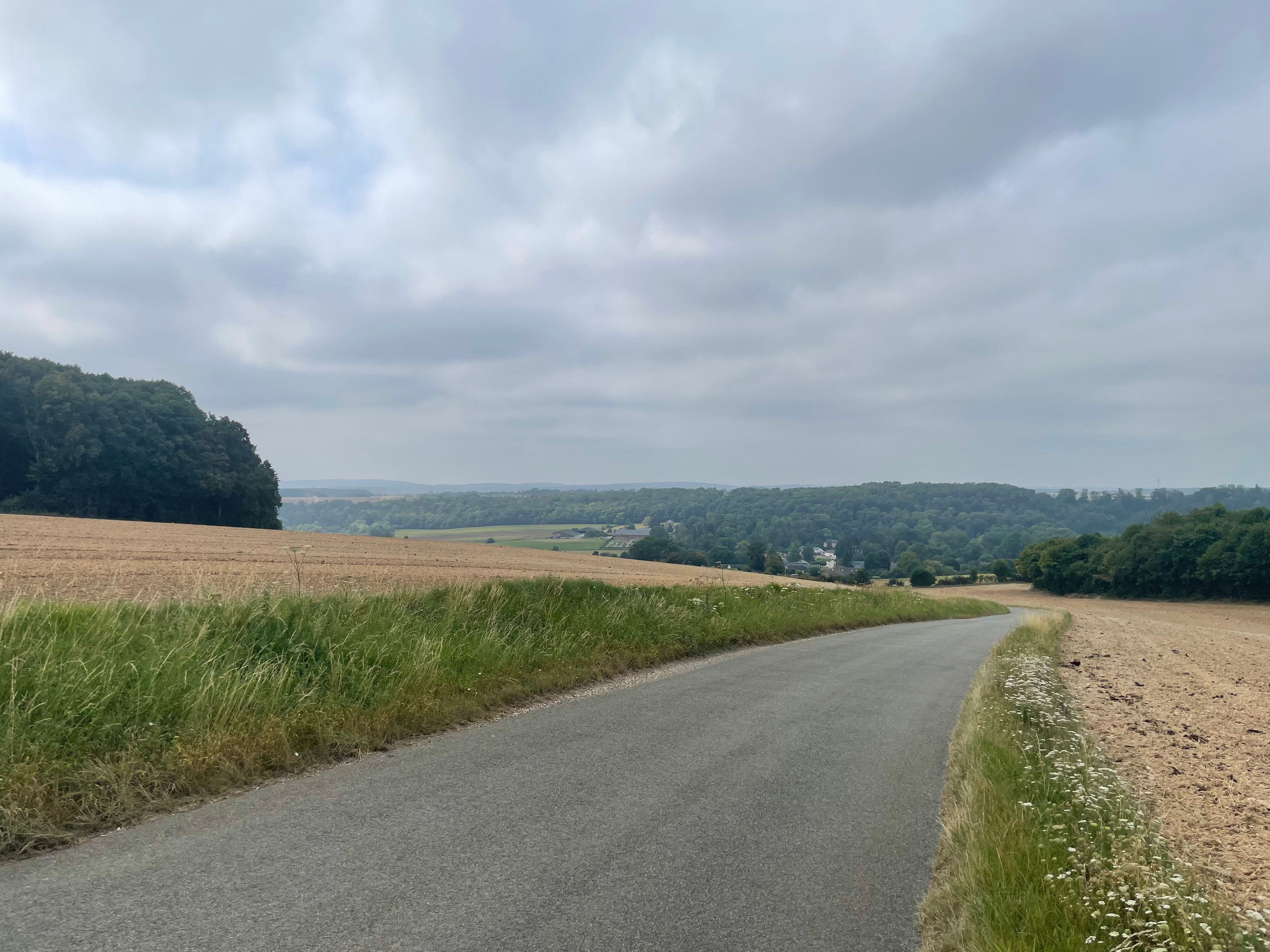 Une petite route de campagne qui descent se perd vers l'horizon. Des champs au premier plan, un paysage de bocage se devine à l'arrière-plan