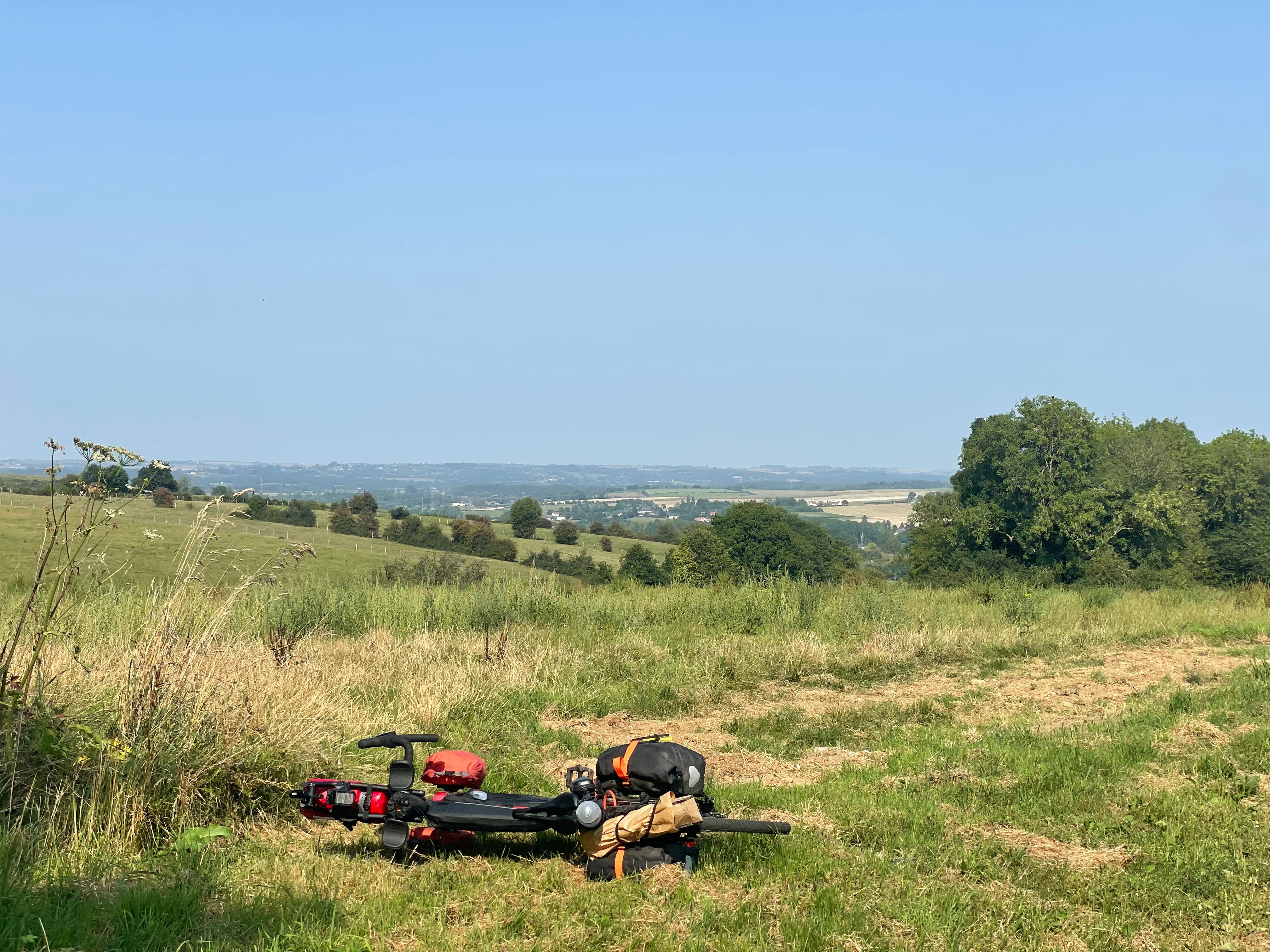 Paysage de bocage sous un soleil de fin d'après-midi. Au premier plan, le vélo est couché sur le flanc