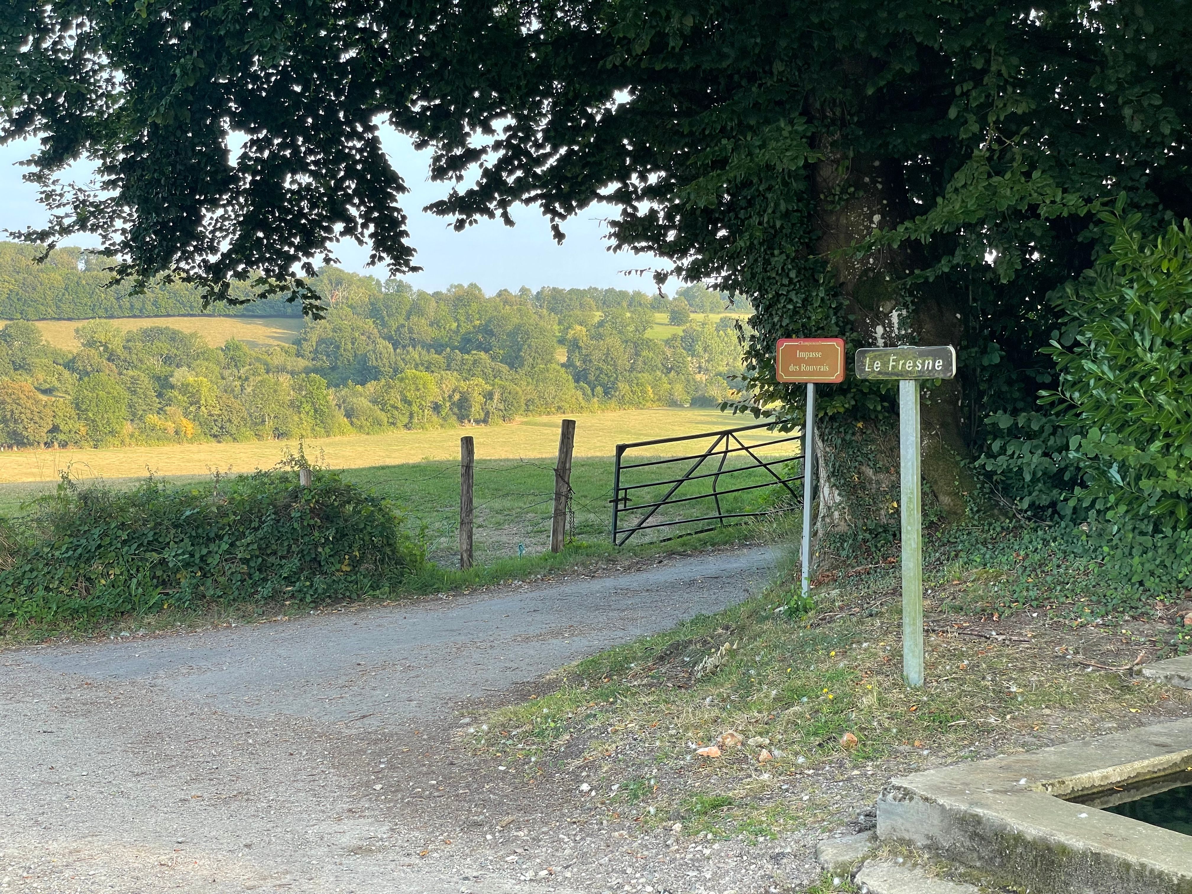 un petit carrefour au premier plan. Des panneaux indiquent: un lieu-dit (Le Fresne) ainsi que le nom de la route qui part sur la droite (impasse des Rouvrais)